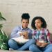 Two mixed race curly girl friends sitting on the couch and watch very scary movie on TV and eat popcorn