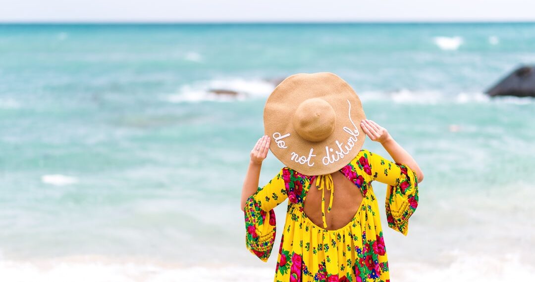 Woman with yellow colorful dress on the beach, wearing a hat that says: do not disturb