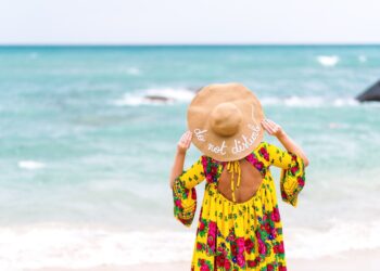 Woman with yellow colorful dress on the beach, wearing a hat that says: do not disturb