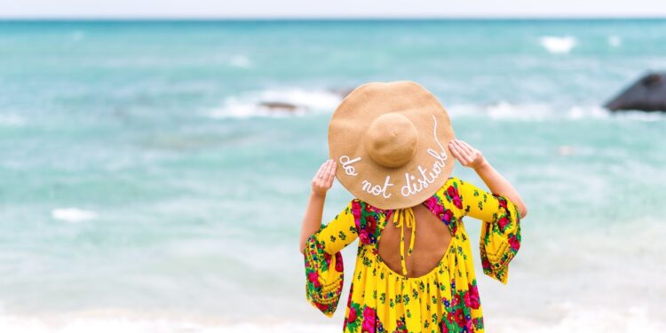 Woman with yellow colorful dress on the beach, wearing a hat that says: do not disturb
