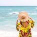 Woman with yellow colorful dress on the beach, wearing a hat that says: do not disturb