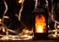 A lit black Ramadan lantern with a mosque design stands against a background of warm bokeh fairy lights.