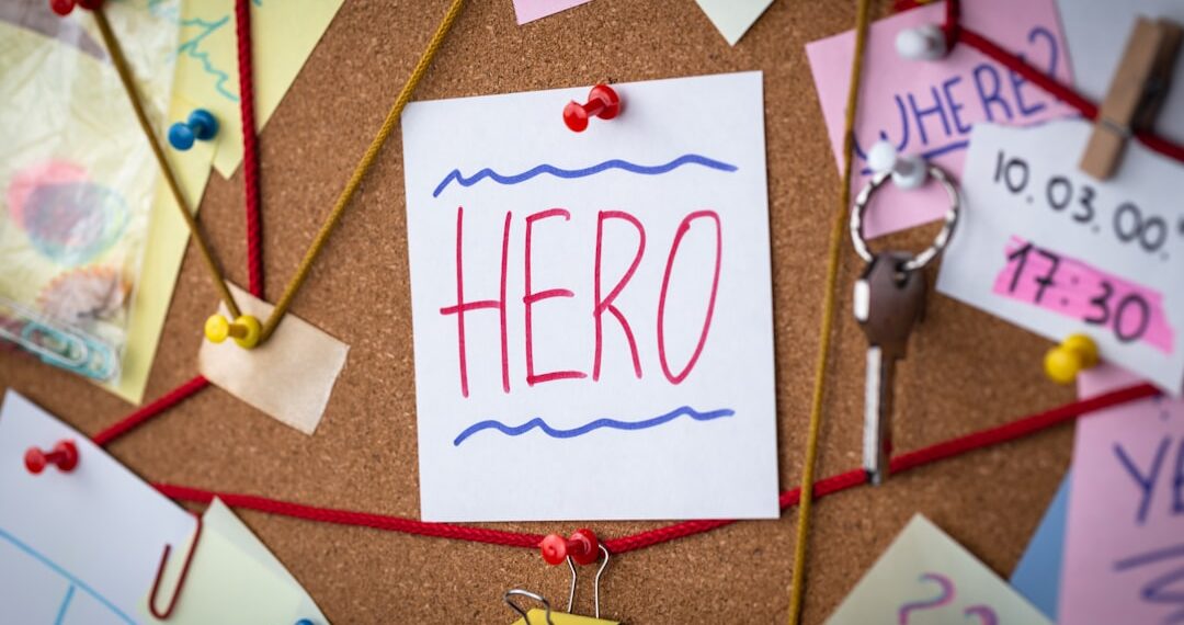 Hero search concept. Close-up view of a detective board with evidence. In the center is a white sheet attached with a red pin with the text Hero.
