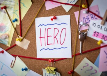 Hero search concept. Close-up view of a detective board with evidence. In the center is a white sheet attached with a red pin with the text Hero.