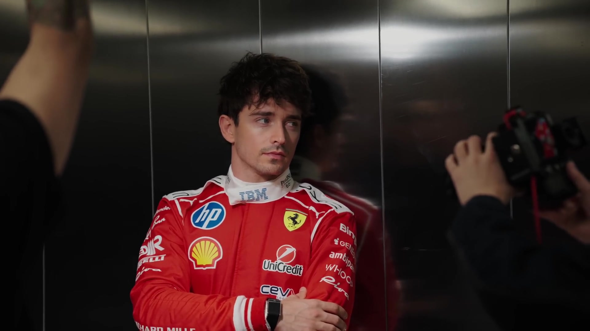 Charles Leclerc in zijn rode Ferrari-racepak met de armen over elkaar in een lift