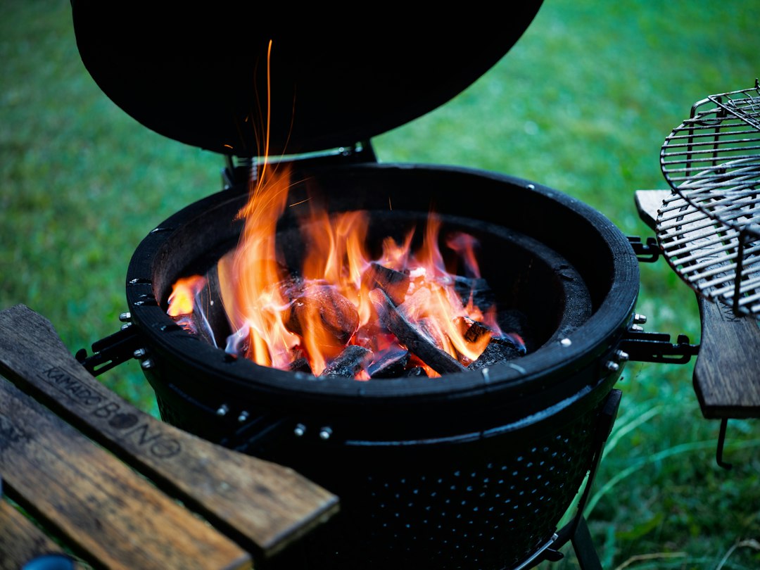 Vlammen boven gloeiende houtskool in een open zwarte keramische kamado op het gras