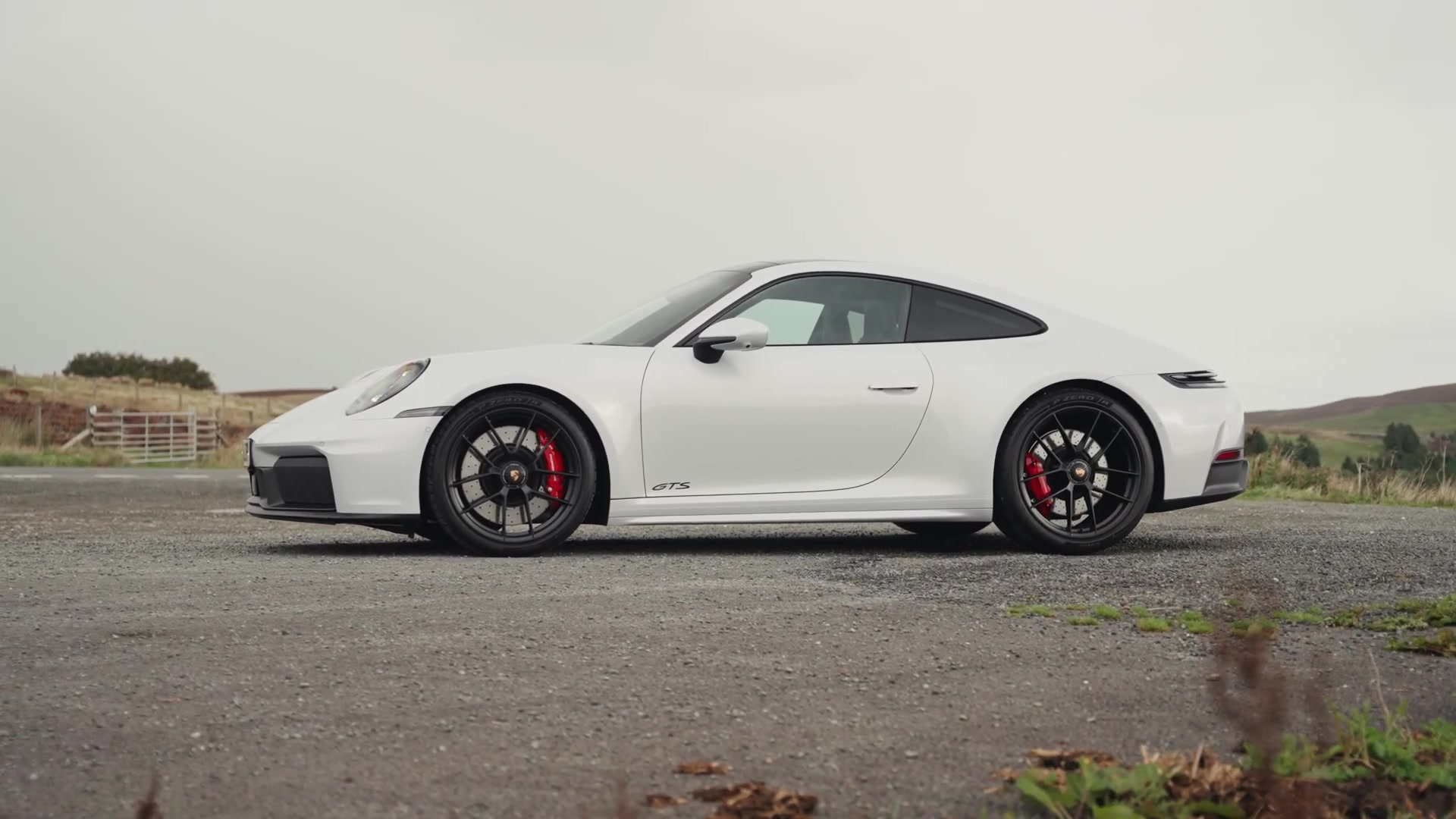 Witte Porsche 911 GTS van opzij op een parkeerplaats in het heuvelland