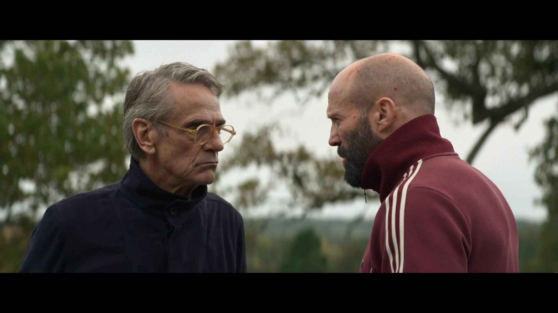 Jeremy Irons en Jason Statham in een rood trainingsjack tegenover elkaar, still uit de teaser van The Beekeeper 2